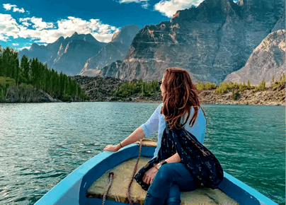 Female traveler sitting on a blue boat cruising on a turquoise mountain lake during a luxury Pakistan holiday tour