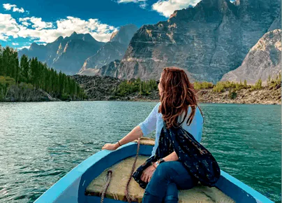 Female traveler sitting on a blue boat cruising on a turquoise mountain lake during a luxury Pakistan holiday tour