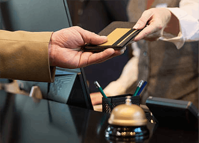 Guest handing a credit card to hotel reception desk next to a brass service bell representing luxury corporate retreat travel bookings
